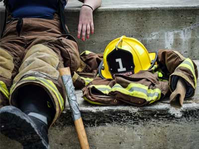 A firefighter sit on a step looks exhausted.